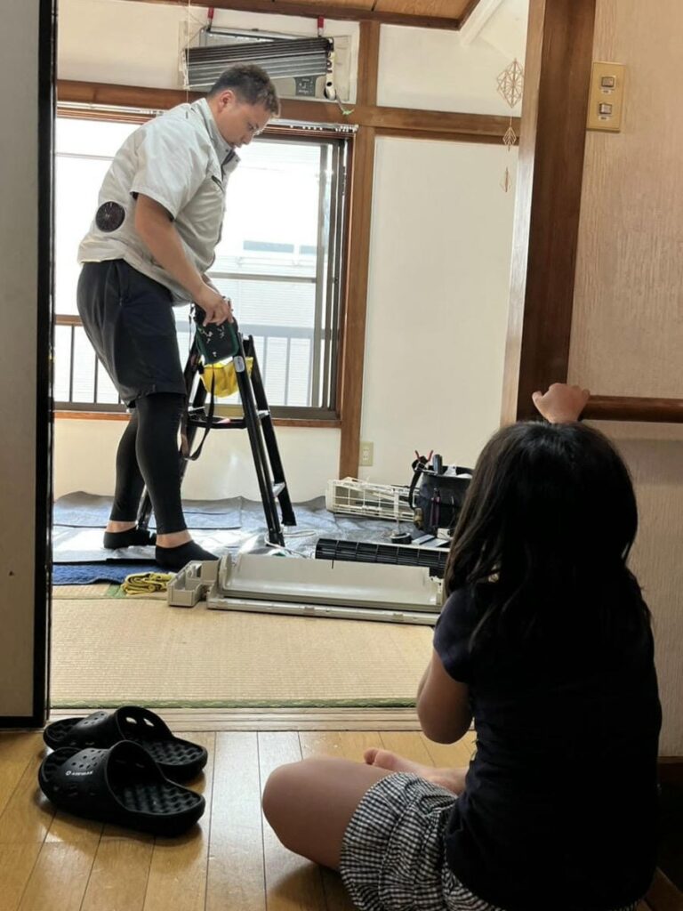 エアコンを完全分解してる作業の様子を見守る子ども