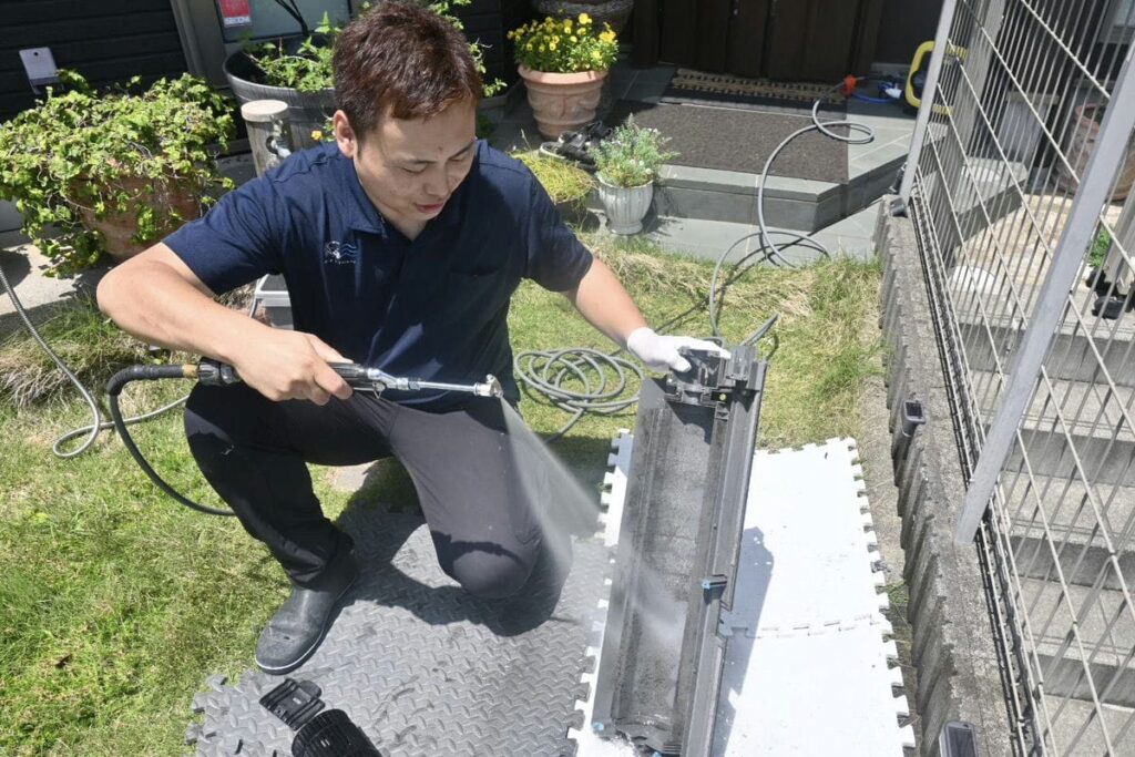 宇賀神がエアコンのケーシングを高圧洗浄機で洗浄をしている様子