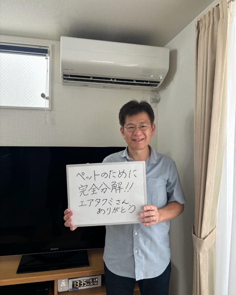T様宅でエアコンの前でホワイトボードを持って笑顔な男性の写真