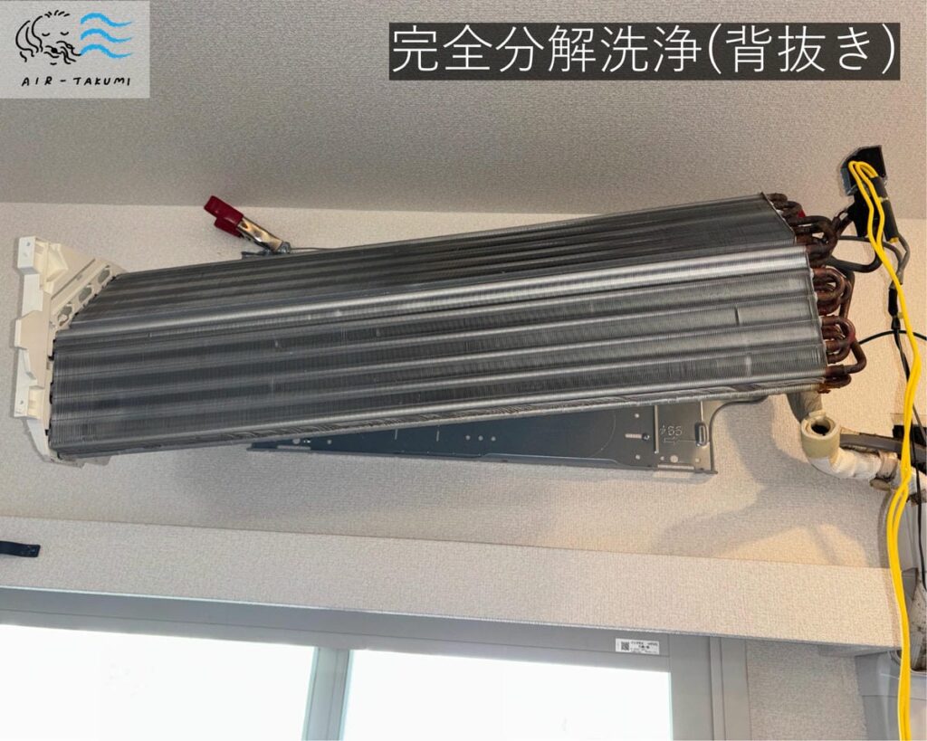 「背抜き」と呼ばれる方法で完全分解洗浄されているエアコン。熱交換器が壁から持ち上げられ、裏側が見えている