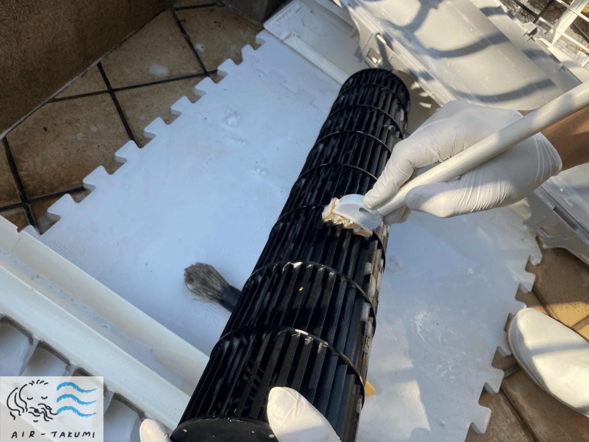 取り外した送風ファンに付着したカビを、ブラシを使って羽根の一枚一枚まで丁寧に手洗いしている場面。