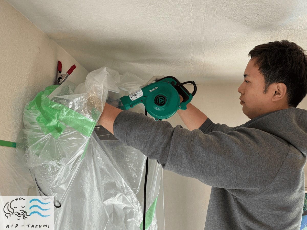 洗浄後の濡れたエアコン内部を、カビの再発防止のため専用のブロワーで強力に乾燥させている作業。